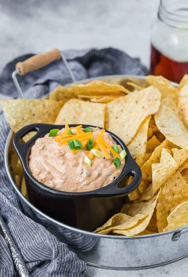 Image of creamy southwestern dip made with cream cheese, sour cream, mayo, green onions, jalapenos, olives, and cheddar cheese. Irresistible! Pictured served on a tray with chips. 