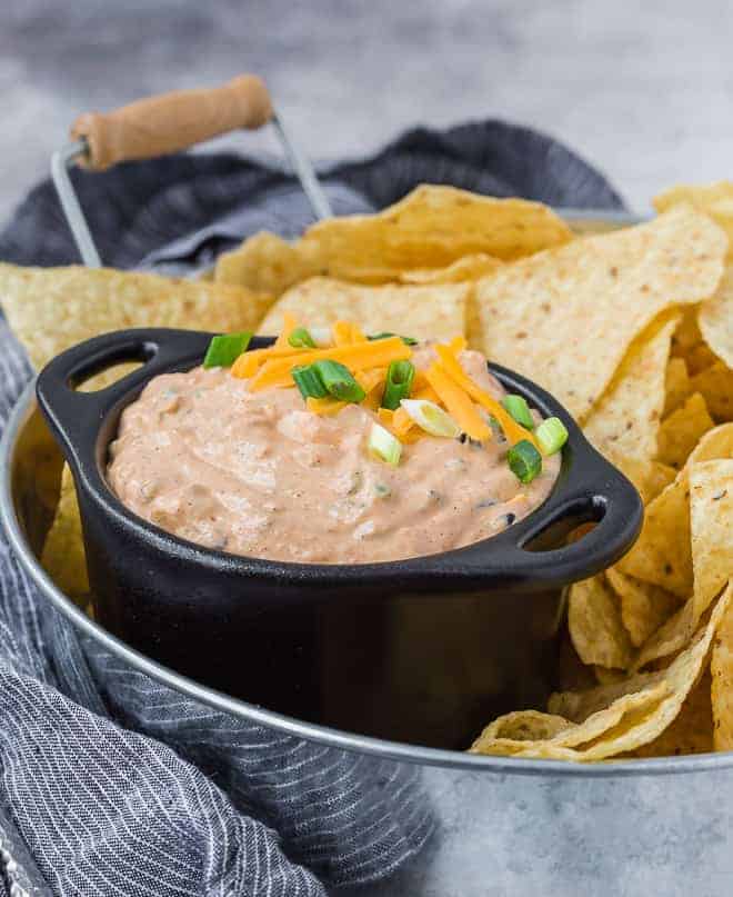 Image of creamy southwestern dip made with cream cheese, sour cream, mayo, green onions, jalapenos, olives, and cheddar cheese. Irresistible! Pictured served on a tray with chips. 