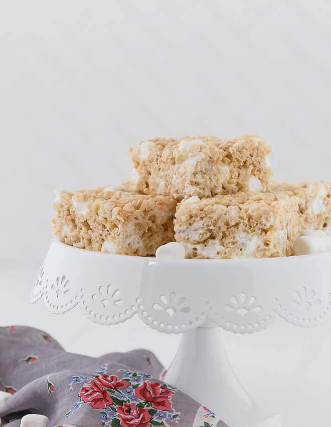 Image of the best rice krispies treats on a small white cake stand. Mini marshmallows are scattered around.