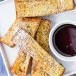 Overhead view of air fryer french toast sticks on a white plate with a bowl of maple syrup for dipping.