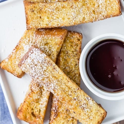 Overhead view of air fryer french toast sticks on a white plate with a bowl of maple syrup for dipping.