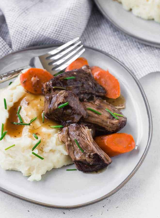 Image of Instant Pot Pot Roast on a plate with carrots, mashed potatoes, gravy and a fork.