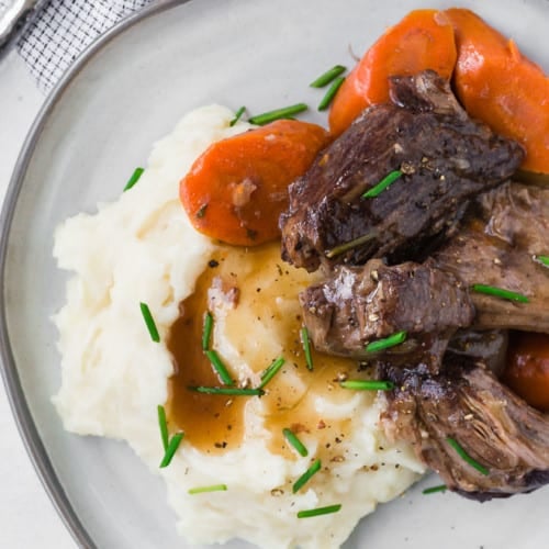 Image of pot roast piled on top of mashed potatoes. Carrots also pictured.