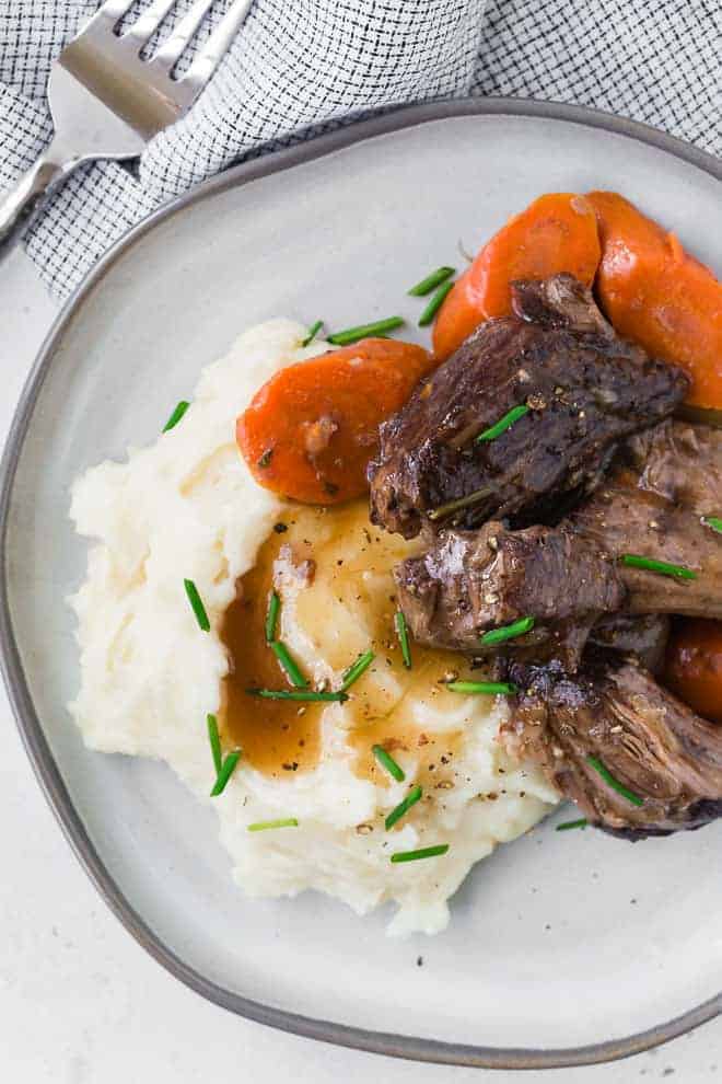 Image of pot roast piled on top of mashed potatoes. Carrots also pictured. 