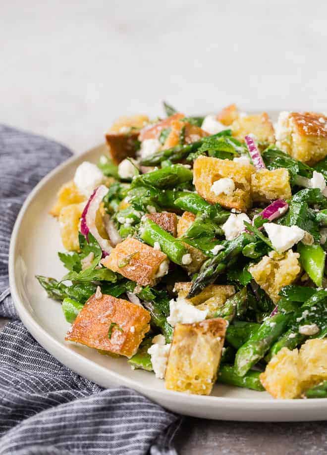 Image of a panzanella salad made with croutons, asparagus, mint, parsley, feta, red onion, and red wine vinaigrette.