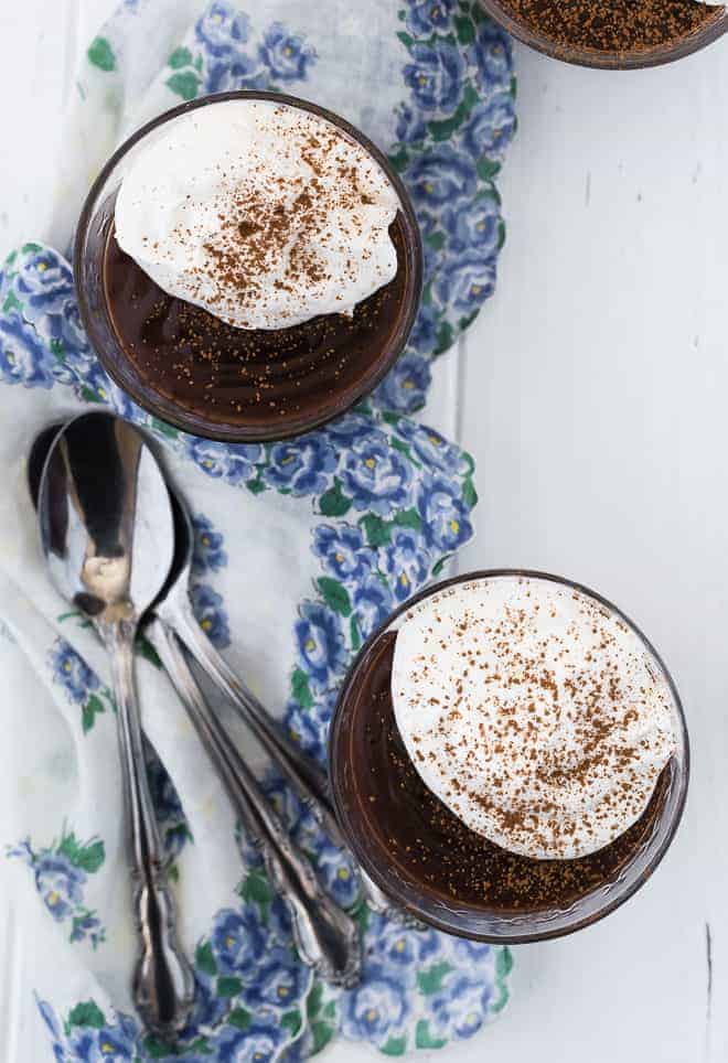 Image of three bowls of chocolate pudding, topped with whipped cream and a sprinkle of cocoa powder. Three spoons are also in the image.