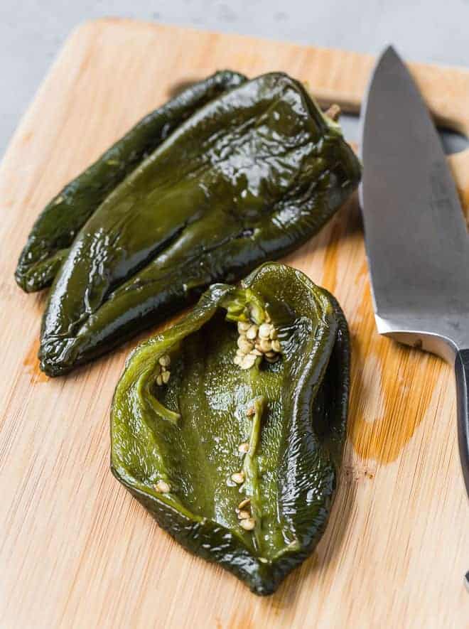 Image of roasted poblano peppers that have been peeled. One has been cut open to show the inside.