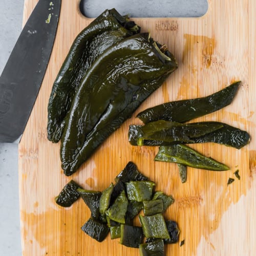 Image of roasted poblano peppers, two whole, one cut in a two different ways (strips, diced).