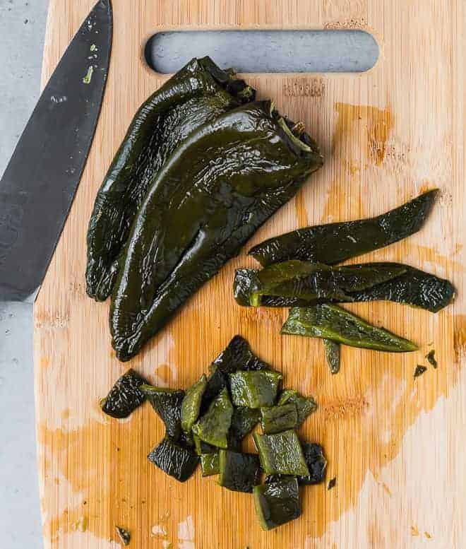 Image of roasted poblano peppers, two whole, one cut in a two different ways (strips, diced). 