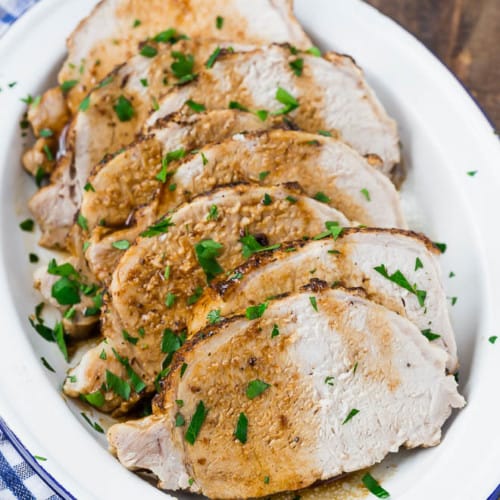 Image of pork loin roast on a blue and white plate on a wooden background.