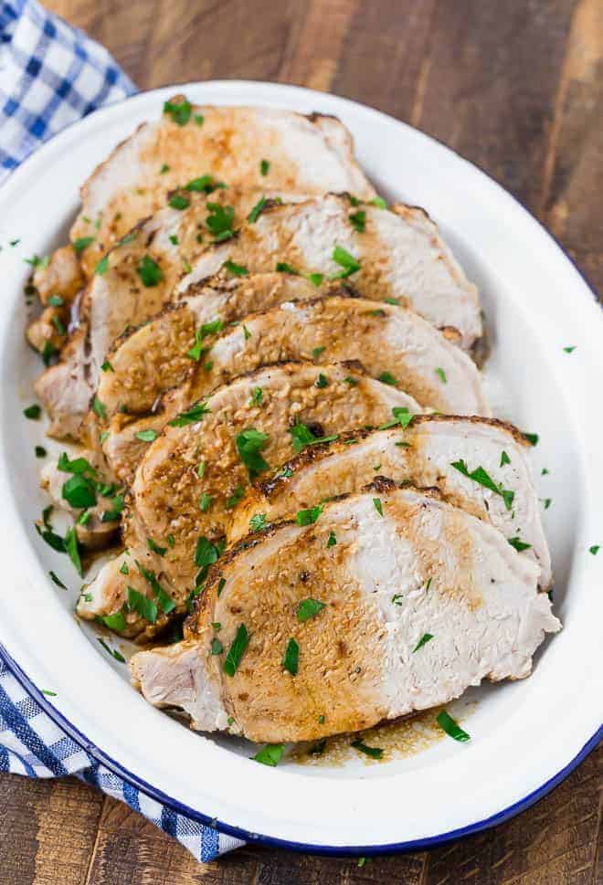 Image of pork loin roast on a blue and white plate on a wooden background.