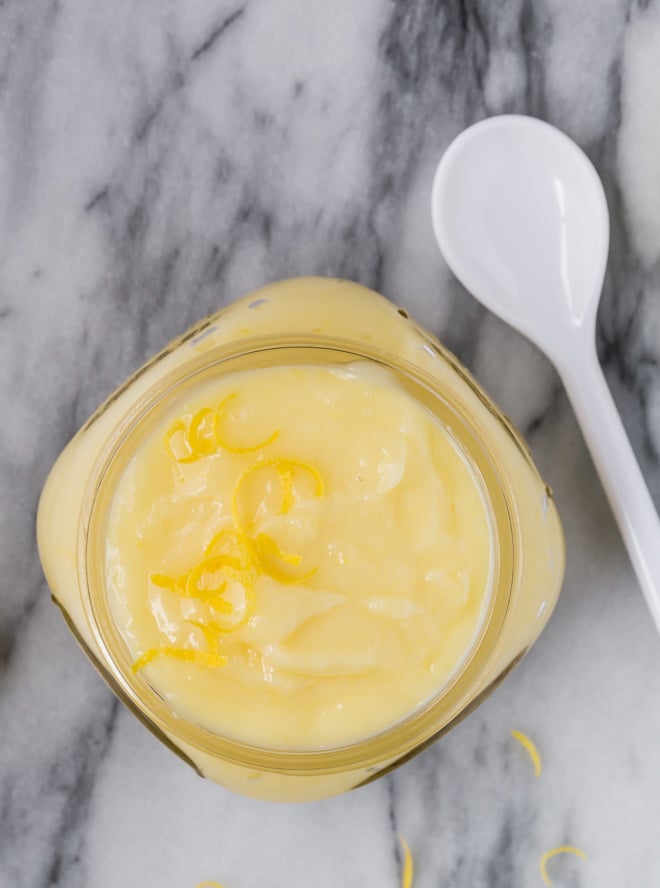 Image of pale yellow lemon cake filling in a small jar with a white spoon next to it.