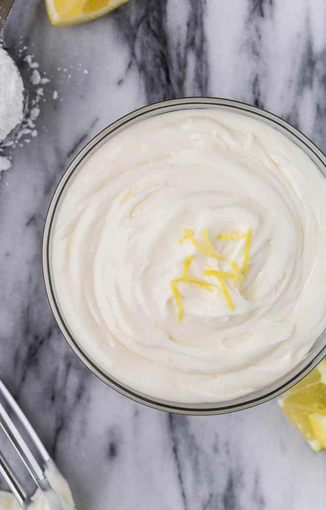 Image of creamy lemon frosting in a large glass bowl, topped with lemon zest. 