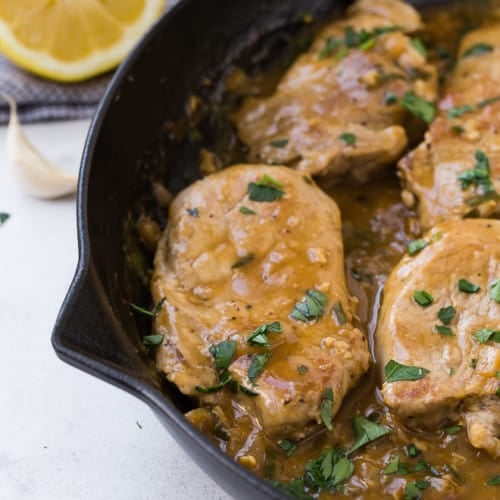 Image of pork medallions in a cast iron frying pan, with a brown sauce, garnished with fresh parsley.