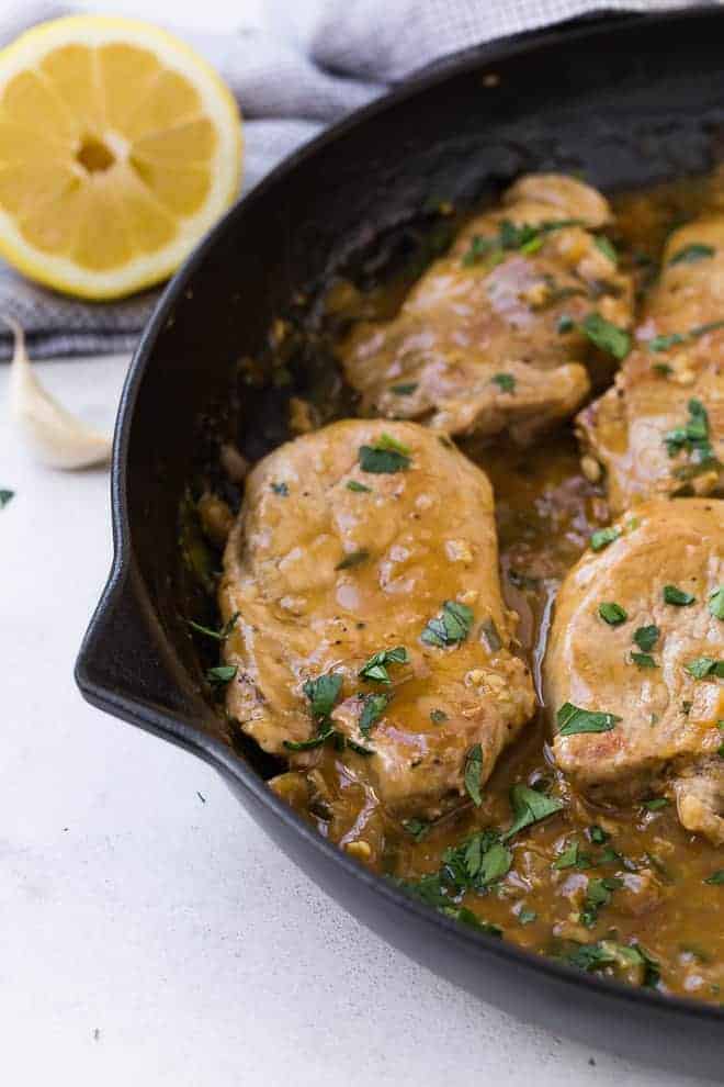 Image of pork medallions in a cast iron frying pan, with a brown sauce, garnished with fresh parsley.