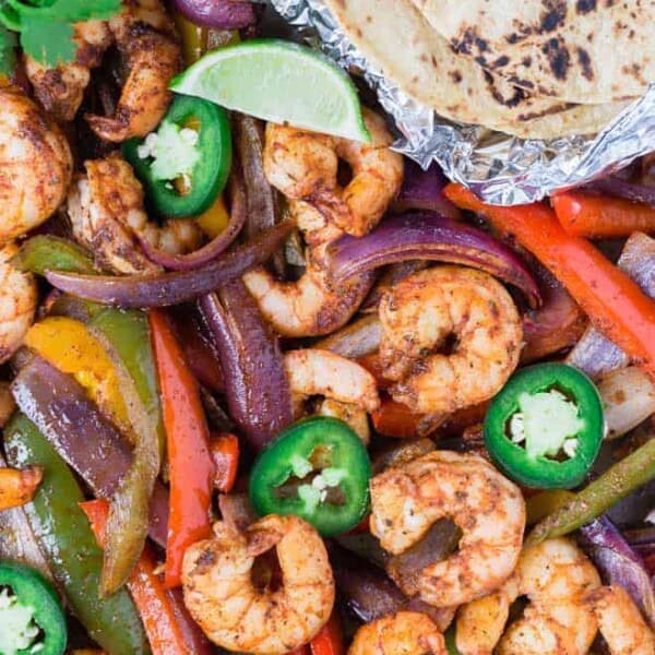 Colorful shrimp fajitas on a sheet pan with tortillas, limes, jalapeno, and cilantro.