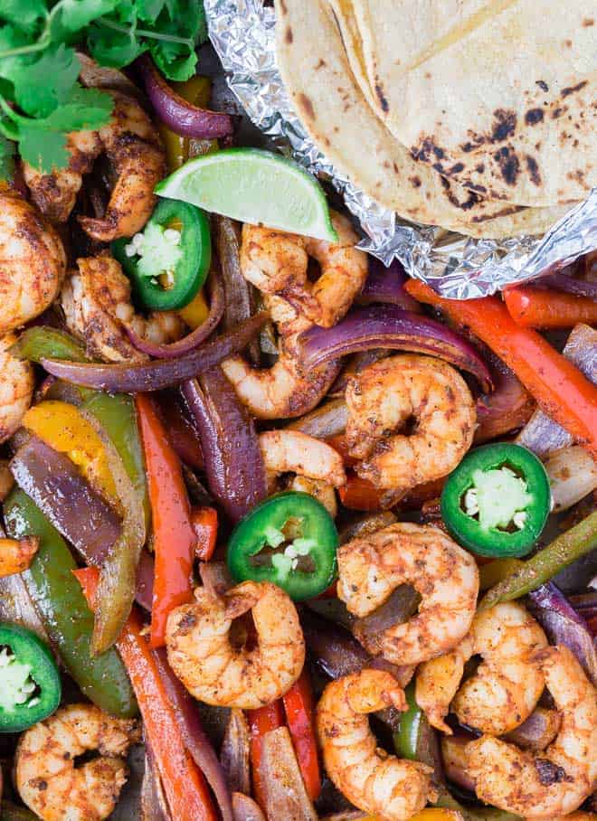 Colorful shrimp fajitas on a sheet pan with tortillas, limes, jalapeno, and cilantro.