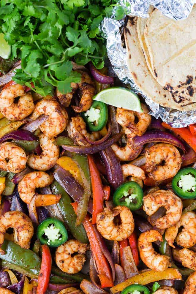 Colorful bell peppers and shrimp on a sheet pan with foil-wrapped tortillas, cilantro, lime and jalapeno. 