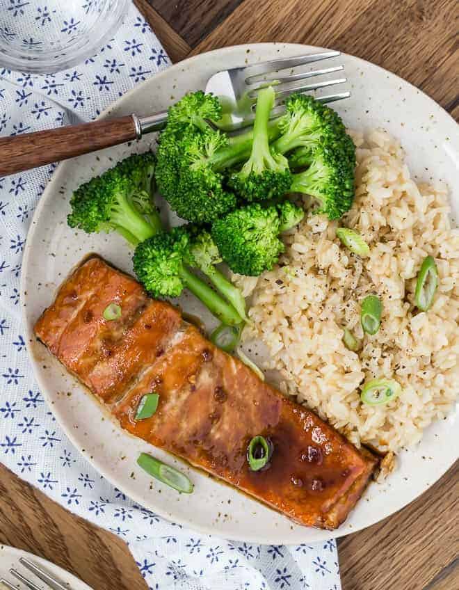 Image of glazed salmon on a plate with brown rice and broccoli. It's all garnished with sliced green onions.
