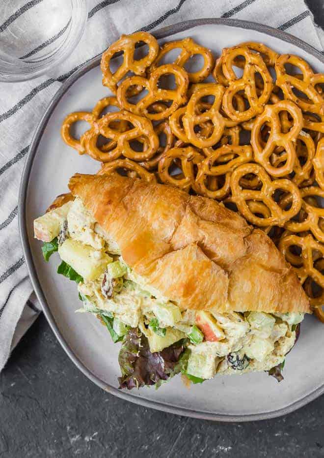 Overhead image of curried chicken salad on a croissant, on a plate with mini pretzels.