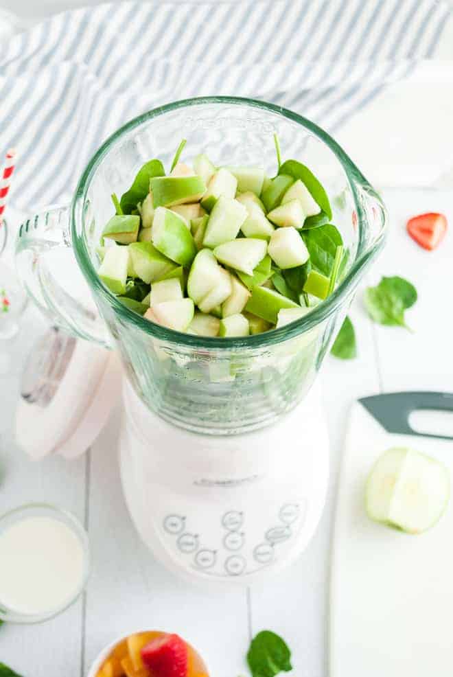 Overhead view of a white blender filled with greens and chopped green apples.