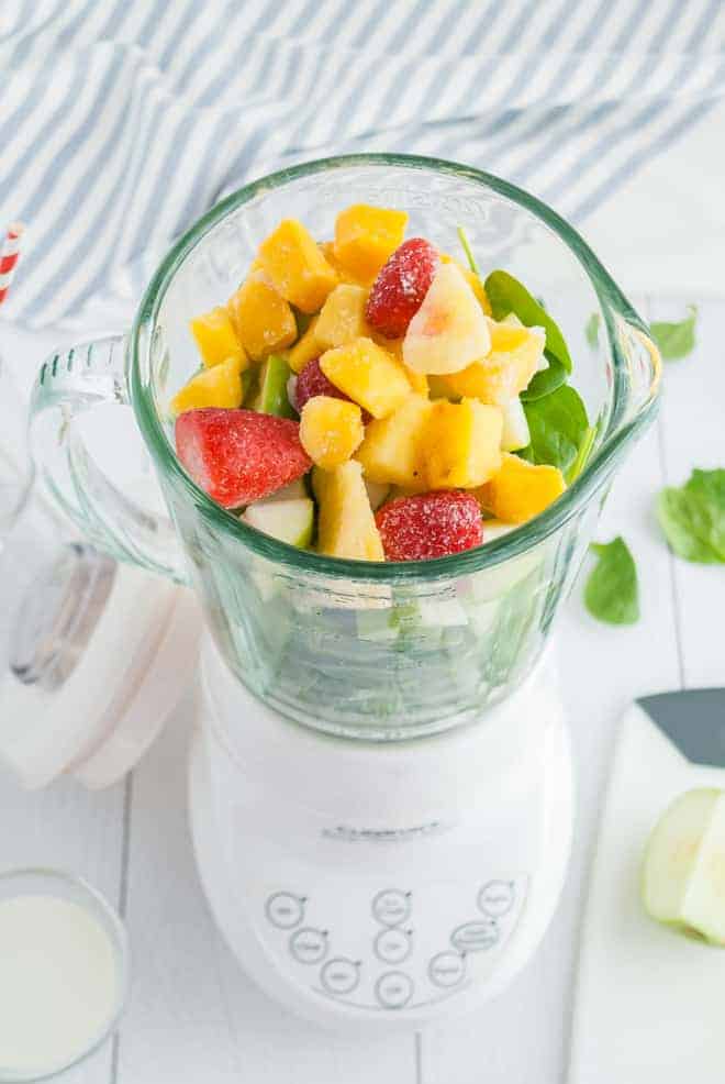 Overhead view of a blender filled with greens and frozen tropical fruit.