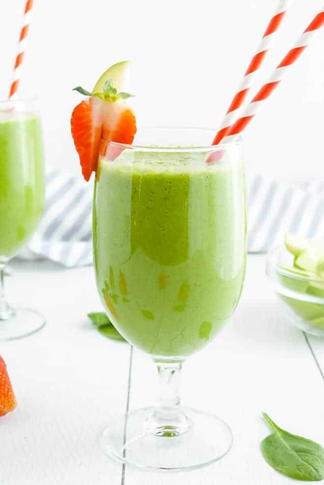 Green smoothie drink in a stemmed glass with two red and white striped paper straws.