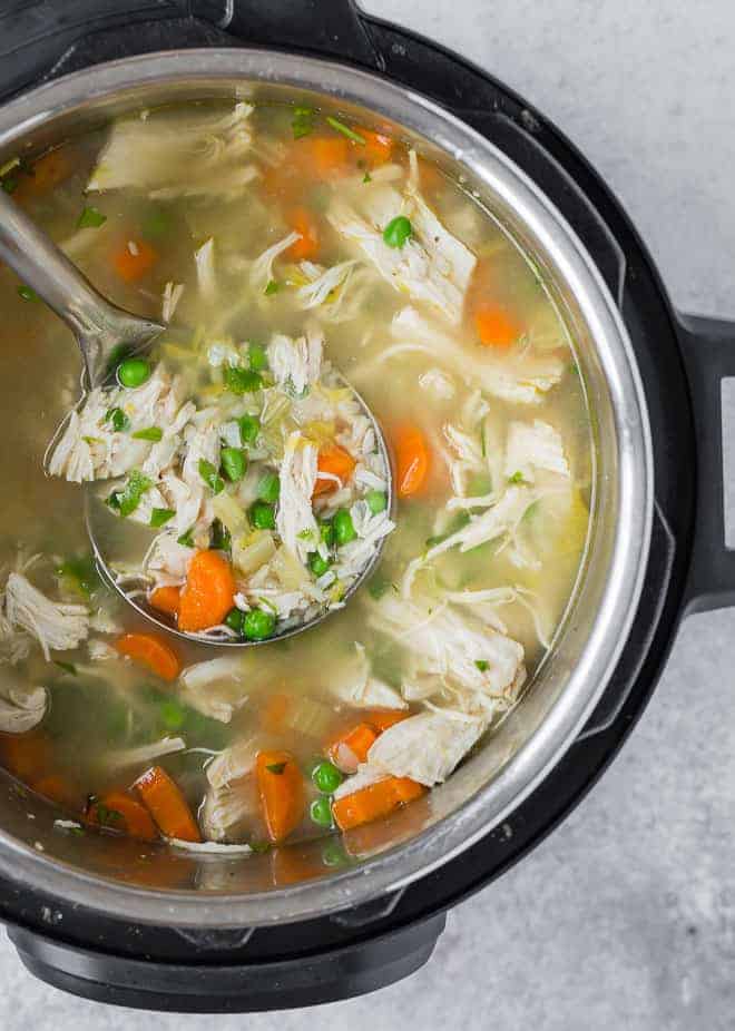 Overhead view of an Instant Pot pressure cooker filled with chicken, rice, and vegetable soup. A ladle is scooping out some of the soup.