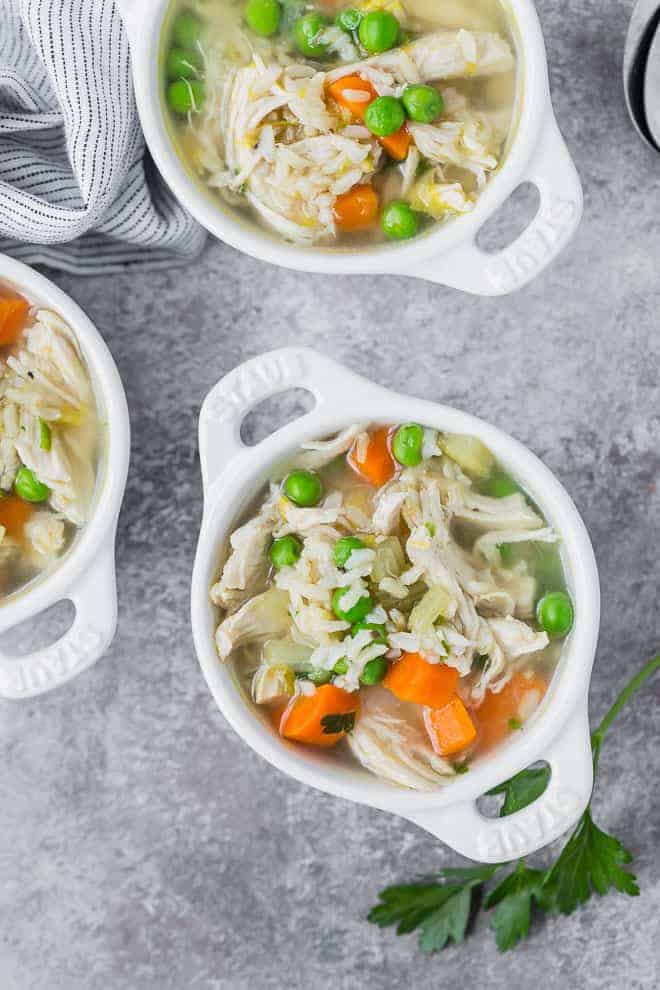Three small glass white bowls full of chicken soup with rice and vegetables.