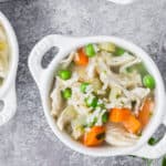 Overhead view of chicken rice soup in a small white bowl with two little handles. Two other bowls of soup are partially pictured.
