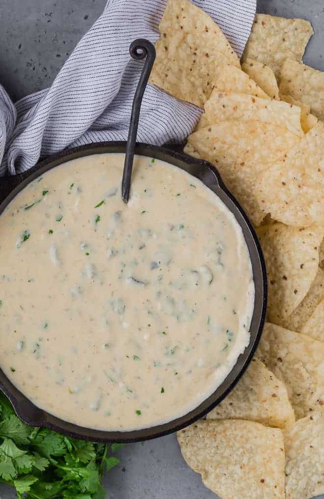 Overhead view of queso made with poblano peppers, in a pan. Next to it are chips and fresh cilantro. 