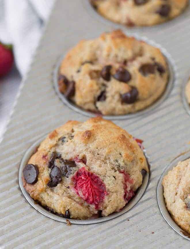 Image of muffins in a tin, flecked with strawberries and chocolate chips. 