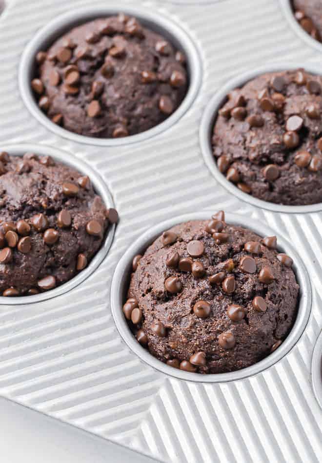 Chocolate muffins in a muffin tin, sprinkled with mini chocolate chips.