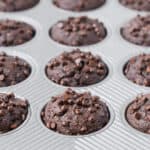 A muffin pan full of whole wheat chocolate muffins, sprinkled with mini chocolate chips.