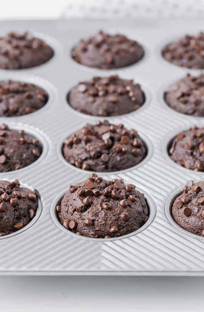 A muffin pan full of whole wheat chocolate muffins, sprinkled with mini chocolate chips. 