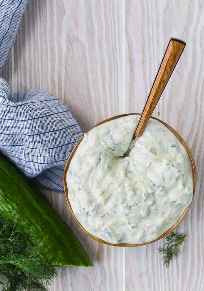 Overhead view of a bowl of homemade tzatziki sauce in a brown-rimmed bowl on a wooden background.