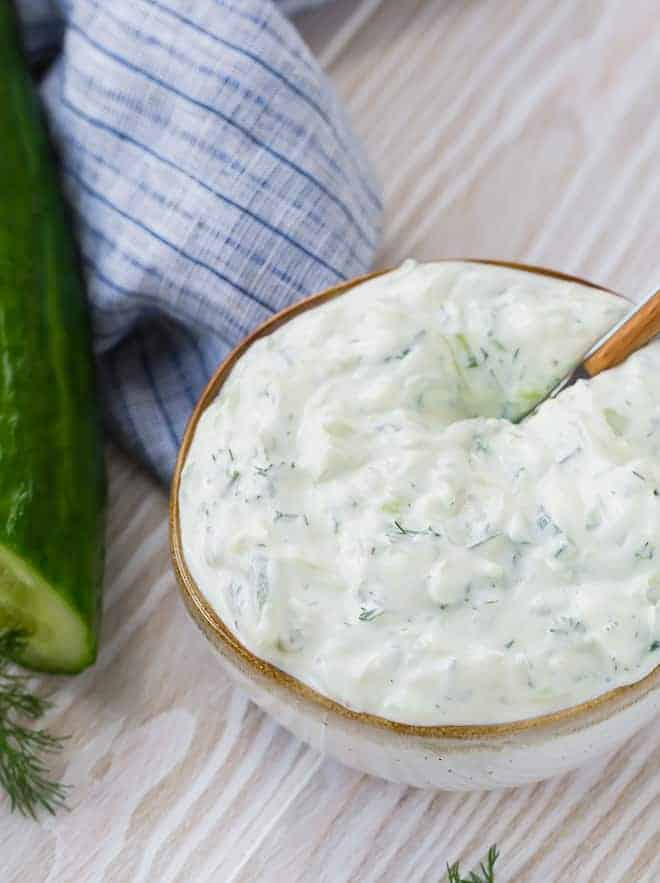 Creamy yogurt and cucumber sauce made with fresh dill in a speckled white bowl with a brown rim.