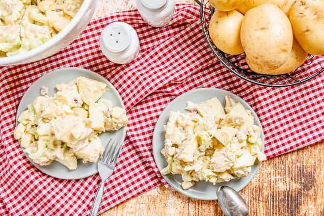 Two plates of creamy mayonnaise mustard potato salad on a red and white checkered cloth.