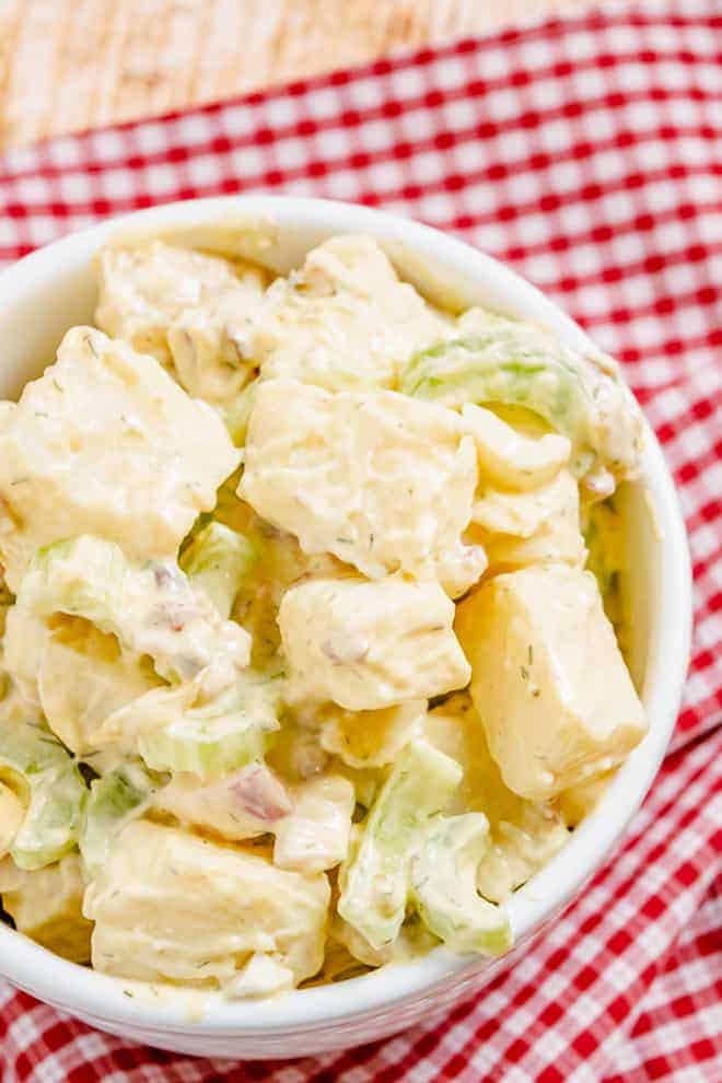 Close up overhead view of a bowl of diced potatoes, celery, onion, bacon, and boiled eggs tossed in a creamy light yellow dressing with flecks of green.