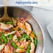 Overhead view of a wok filled with white rice, chicken, sugar snap peas, carrots, and red onions in stir fry form. It is garnished with fresh basil ribbons.