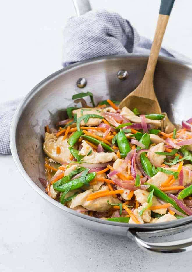 Colorful stir fry in a silver wok pan with a wooden spoon.
