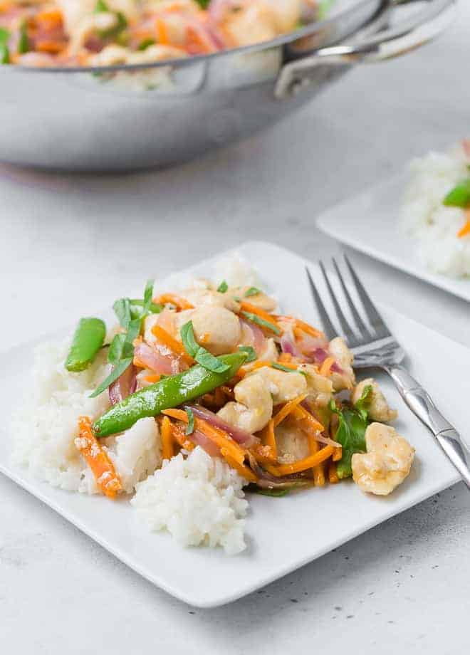 White plate filled with white rice, chicken, sugar snap peas, carrots, and red onions in stir fry form. It is garnished with fresh basil ribbons.