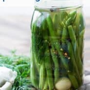 Glass jar of green beans, and a clove of garlic, in a clear liquid. Text overlay reads "super easy pickled green beans"