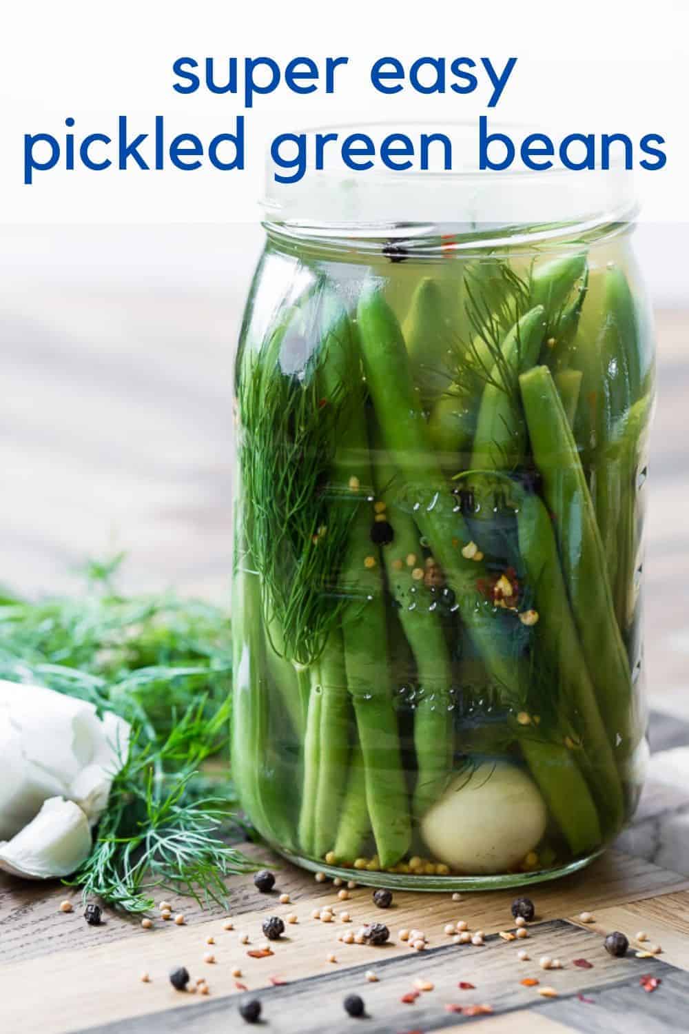 Glass jar of green beans, and a clove of garlic, in a clear liquid. Text overlay reads "super easy pickled green beans"