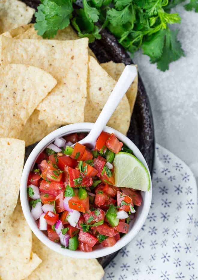 Overhead view of pico de gallo in a white bowl, surrounded by tortilla chips. 