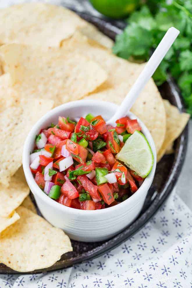 Small white bowl of pico de gallo surrounded by white tortilla chips.