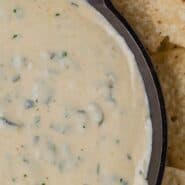 Overhead view of white queso with green specks of poblano peppers.