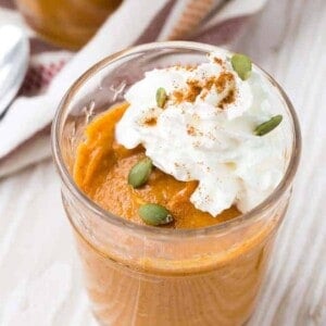 Close up view of easy pumpkin pudding garnished with whipped cream, pepitas, and cinnamon.