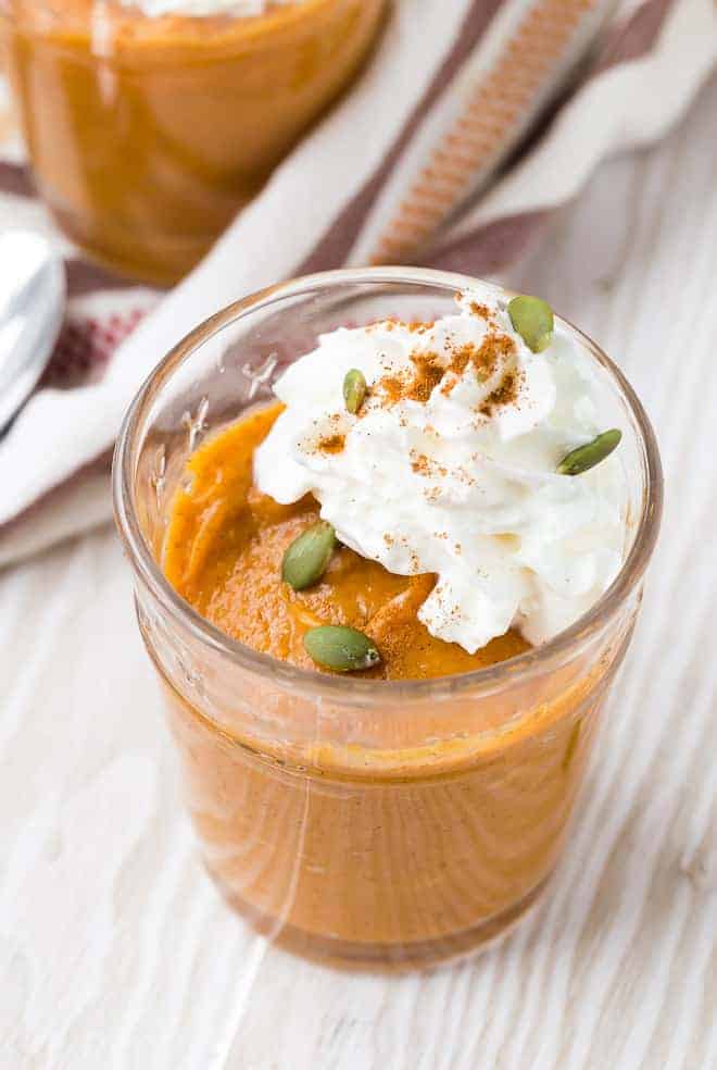 Close up view of easy pumpkin pudding garnished with whipped cream, pepitas, and cinnamon.