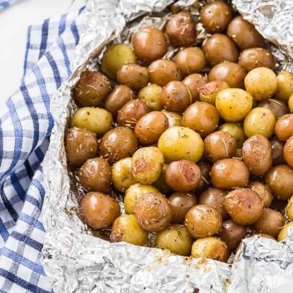 A pound and a half of baby potatoes, partially wrapped in foil. Specks of rosemary are pictured, as well as a blue and white linen.
